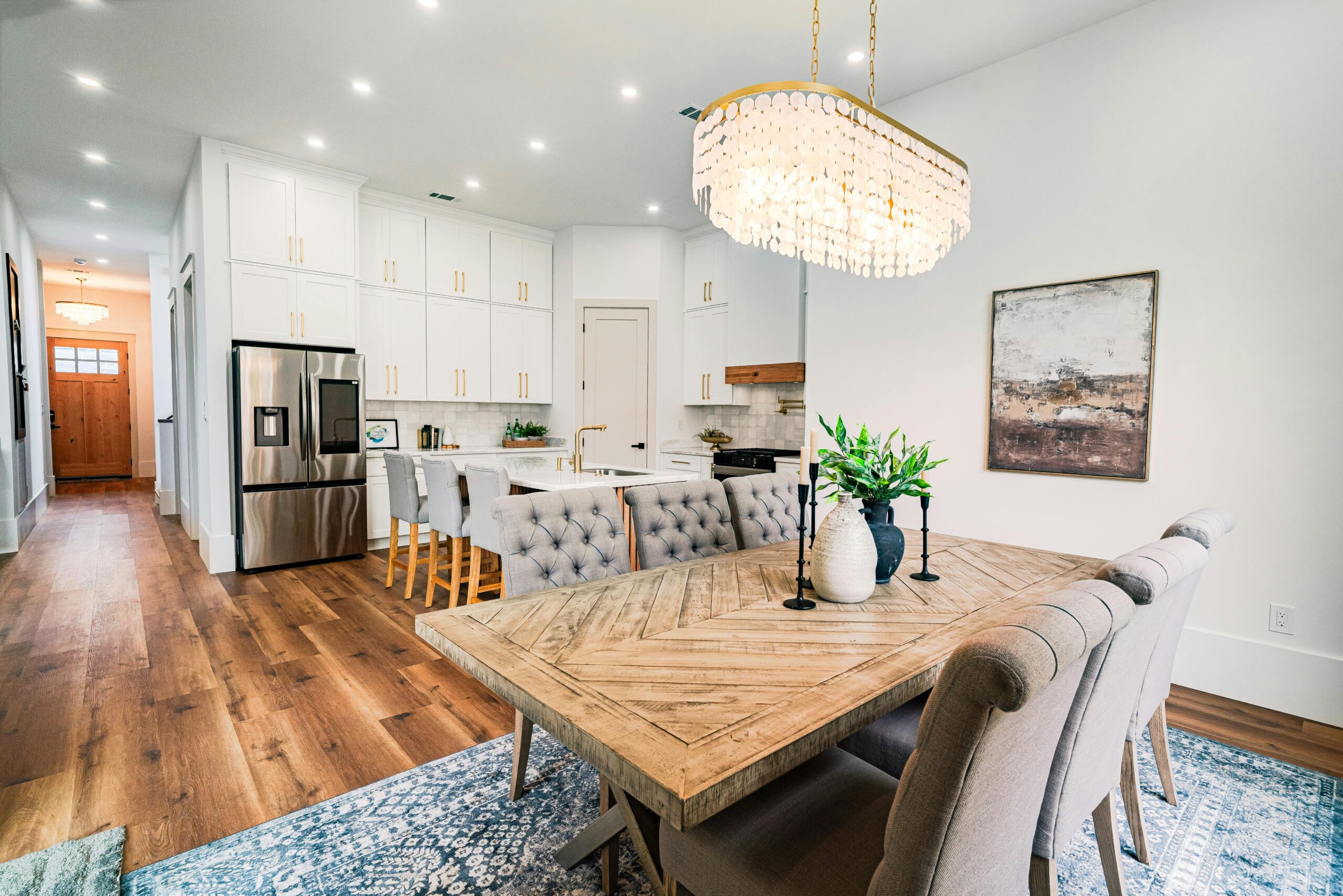 Spacious modern dining area with wooden table, plush chairs, and chandelier in a bright kitchen setting.