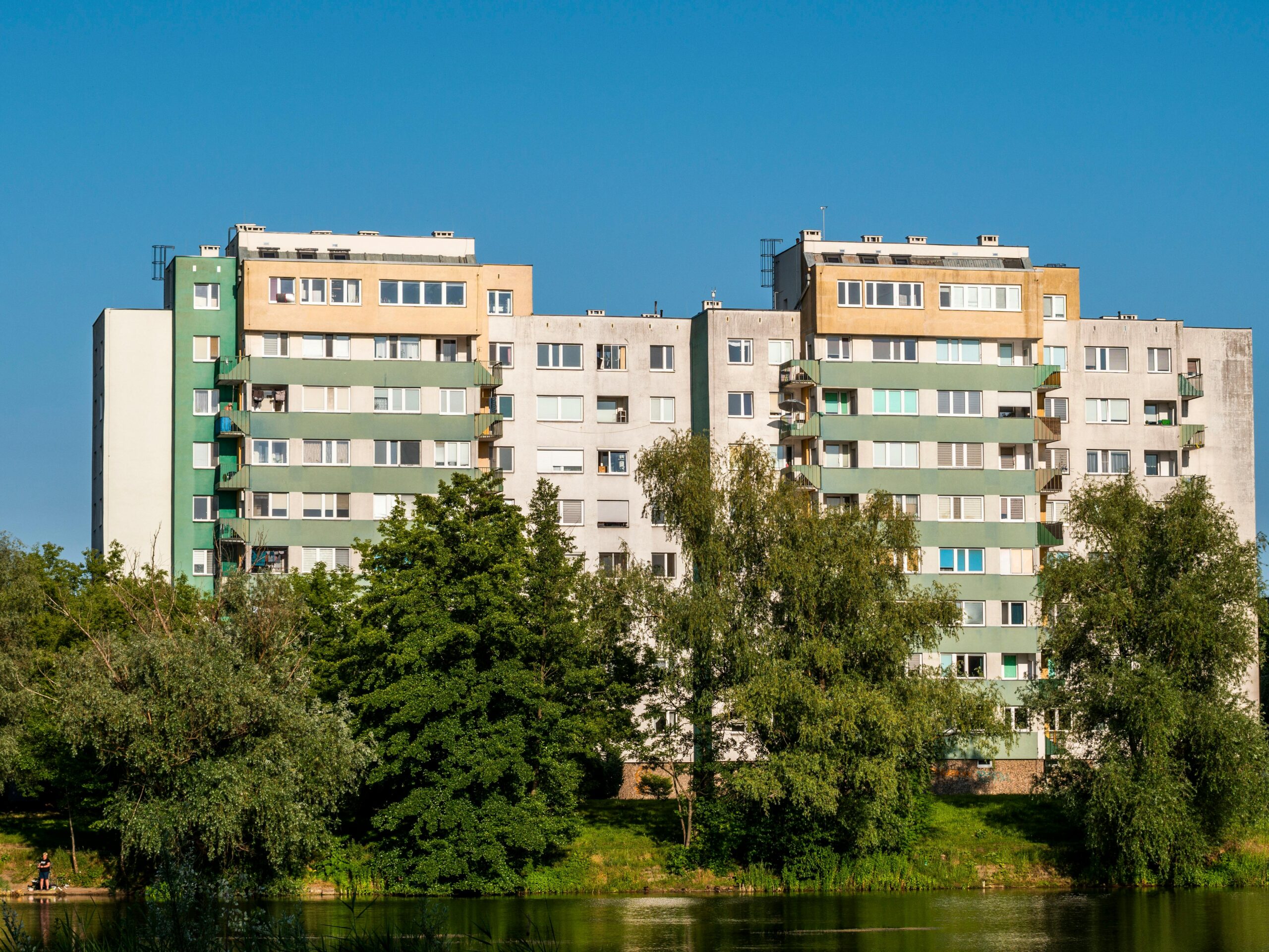 High-rise apartment buildings surrounded by trees under a clear blue sky.