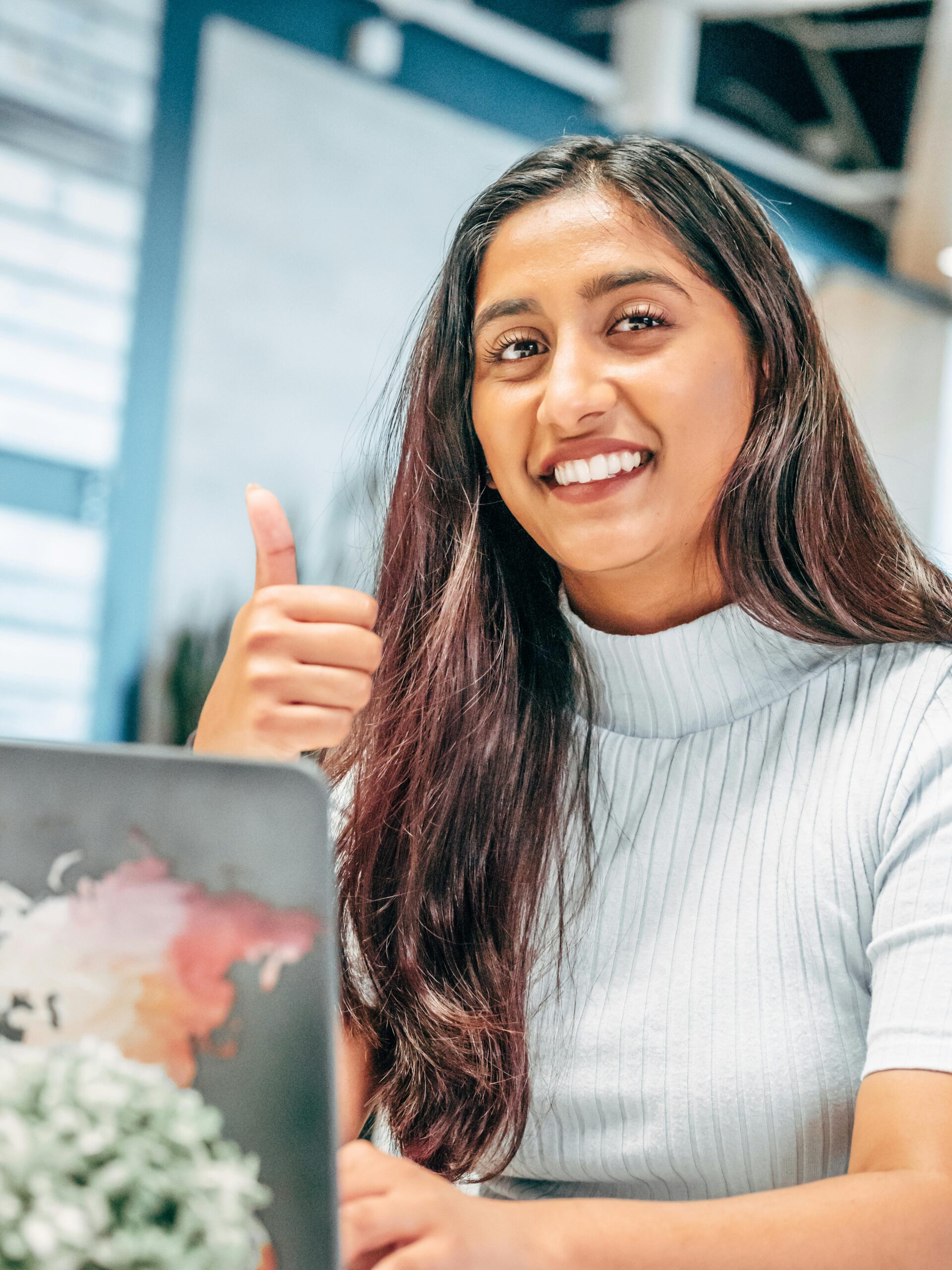 Smiling woman with long hair gives a thumbs up at her desk in a modern office.