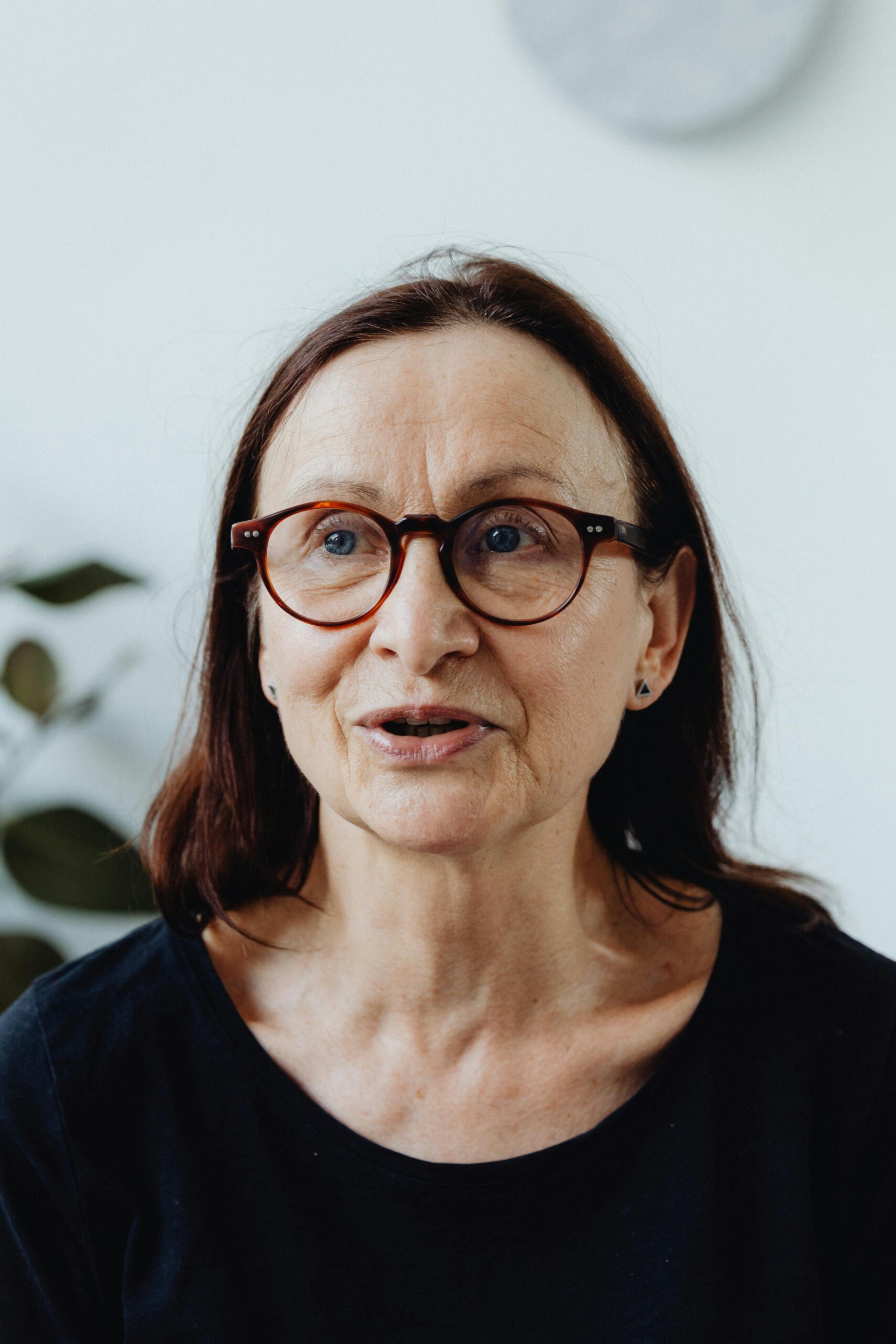 A thoughtful elderly woman wearing glasses, captured in a candid moment indoors.